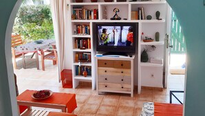 A living room with a TV, bookshelves, and a dining area with a table and chairs. - House with terrace of flowers and solarium, near beaches, A/C, wifi, Sat TV, BBQ (San Juan de los Terreros)