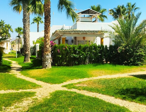 A well-maintained garden with a clear path leading to a white building with a tiled roof and a balcony.