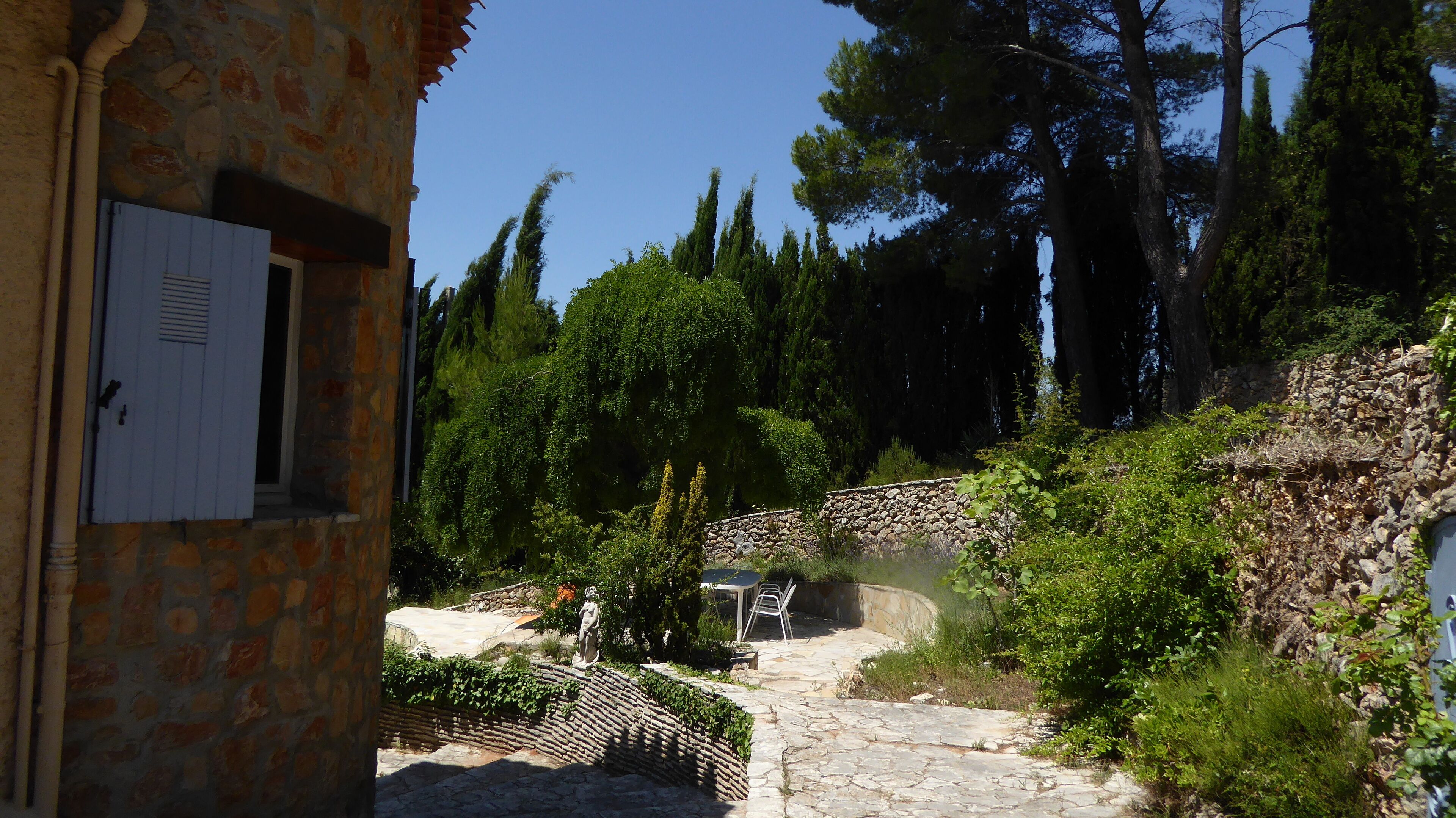 Un edificio de piedra con una puerta y un pequeño espacio exterior con un muro de piedra y una silla.