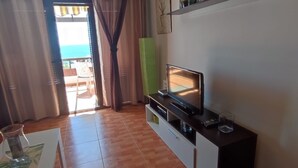 A living room with a wooden floor, a TV on a black stand, a glass table with a vase, and a bookshelf with decorative items. - Quiet apartment near the beach VV-35-3-0002306 (Tías)