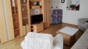 A living room with a TV, wooden furniture, a sofa, and a patterned ottoman.