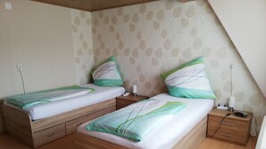 A bedroom with two wooden beds, each with a nightstand and a drawer. The walls have a leaf pattern, and there's a ceiling light.
