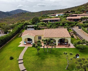 Una villa con techo de tejas, rodeada de céspedes cuidados y árboles, ubicada en un paisaje montañoso.