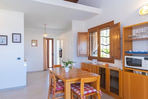 Una cocina con armarios de madera, una mesa de comedor con sillas, un microondas y una ventana con cortinas.