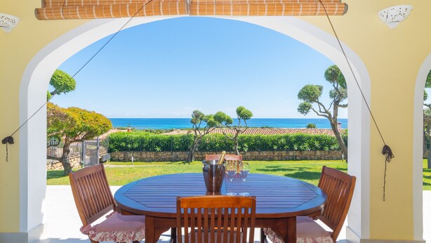 A round wooden table with four chairs, a wooden pergola overhead, and a view of the sea through an archway. - Fantastic holiday apartment with sea view - Villa Nina (San Teodoro)