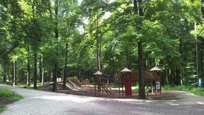 Een speeltuin met een glijbaan en klimconstructies, omgeven door bomen.