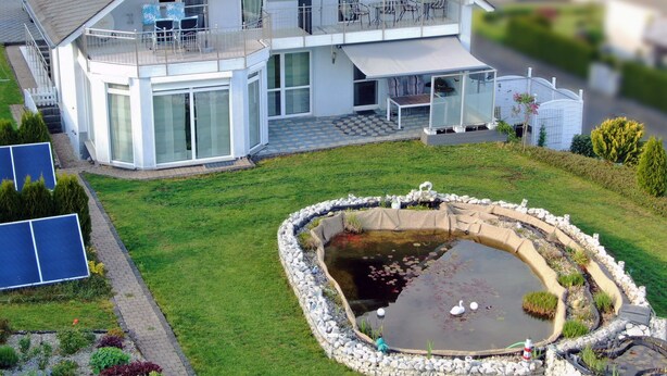 Een woonhuis met twee verdiepingen, een balkon, een vijver en zonnepanelen.