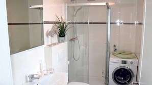A modern bathroom with a glass-enclosed shower, a sink, a toilet, and a built-in washing machine.