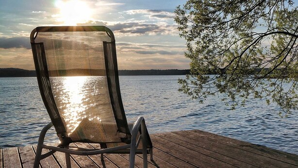 A chair on a wooden deck overlooking a body of water with a sunset in the background.