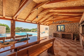 A covered outdoor area with a pool, stone walls, and a wooden table and bench.