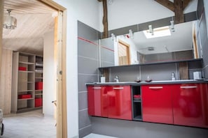 Ein modernes Badezimmer mit roten Schränken, einem großen Spiegel und einer Holzbalkendecke.