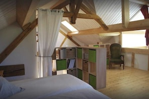 Ein Schlafzimmer mit Bett, Stuhl, Schreibtisch mit Stauraum und einem Fenster mit Vorhängen.