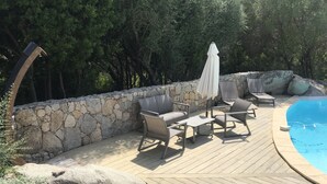 A wooden deck with outdoor furniture, a stone wall, and a swimming pool.