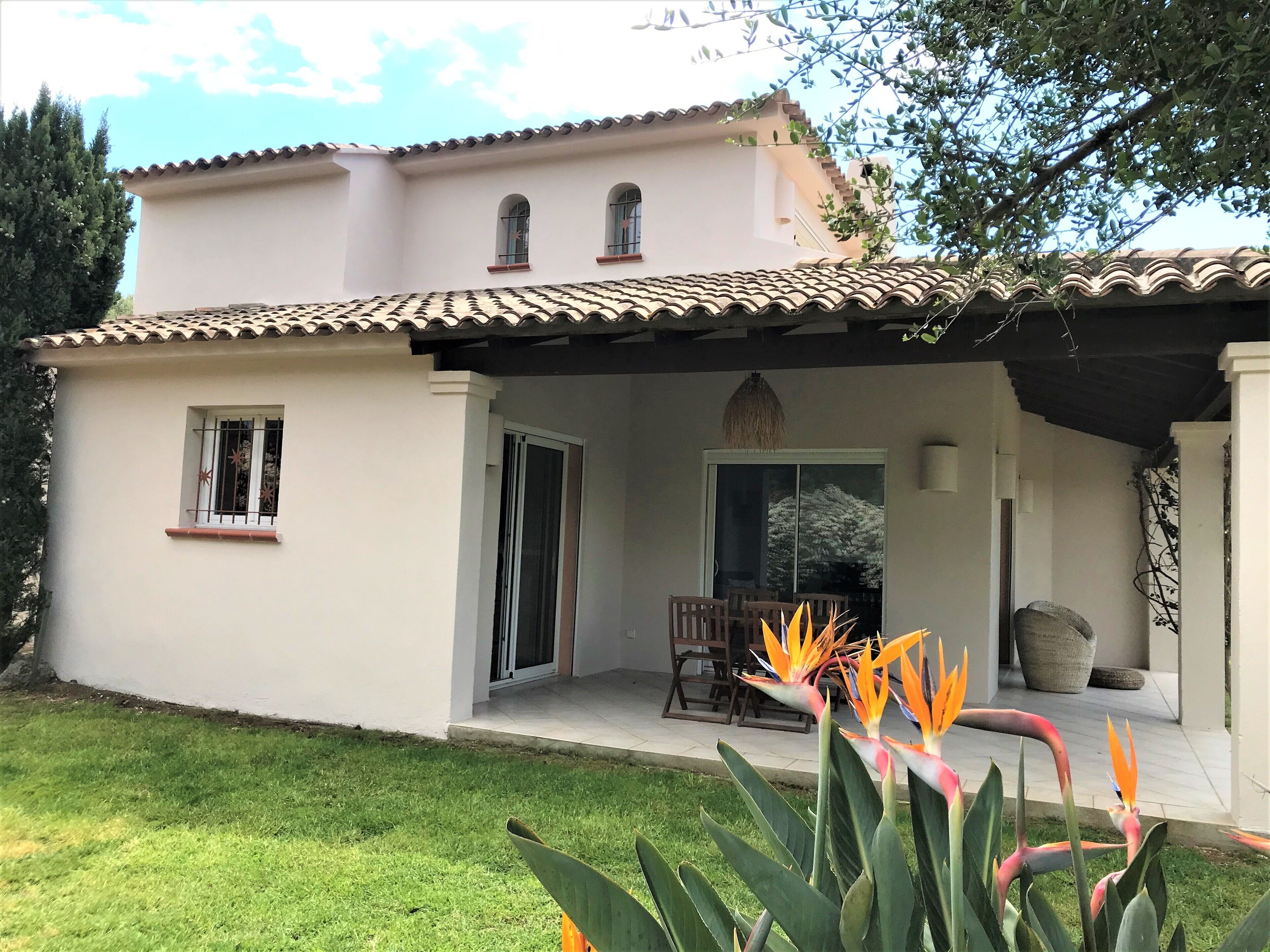 Un bâtiment à deux étages, doté d’un toit recouvert de tuiles, d’un patio abrité avec une table et des chaises, et d’une grande fenêtre.