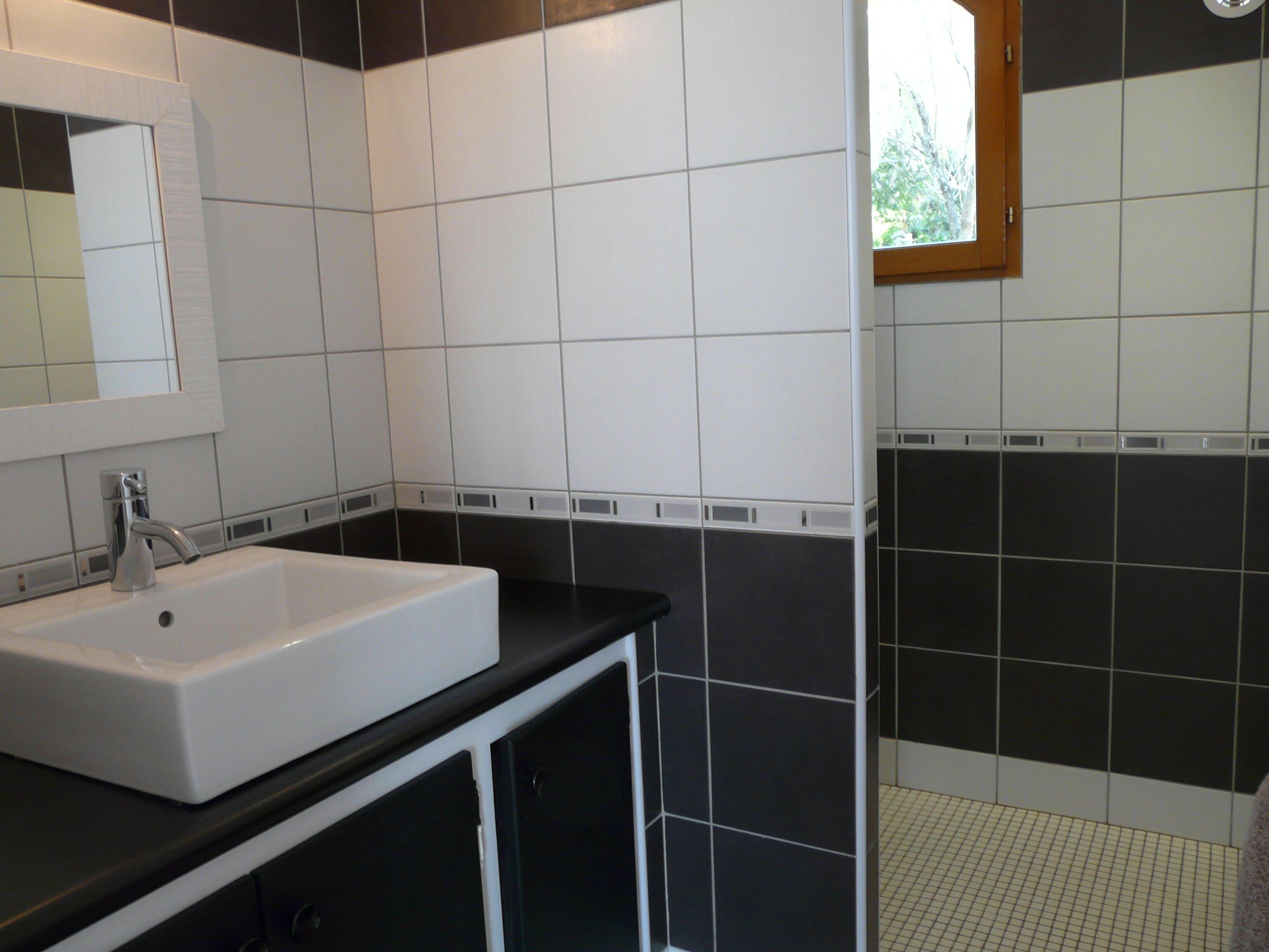 Un baño con lavamanos blanco, encimera negra y paredes con azulejos blanco y negro.