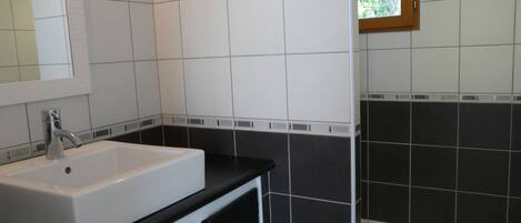 Un baño con lavamanos blanco, encimera negra y paredes con azulejos blanco y negro.