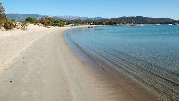 A beach with clear water, a sandy shore, and mountains in the background.