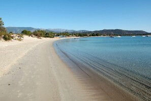 A beach with clear water, a sandy shore, and boats in the distance.