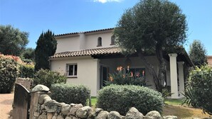 A two-story house with a tiled roof, stone wall, and a garden with various plants and a bird of paradise flower.