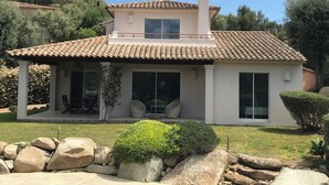 A two-story house with a tiled roof, large windows, and a patio area with outdoor furniture.