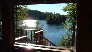 Blick von einem Zimmer mit einer Holterrasse auf einen von Bäumen umgebenen See.