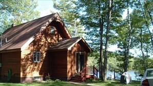 Eine Holzhütte mit Veranda, umgeben von Bäumen und blauem Himmel.