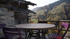 Een houten terras met een ronde tafel en stoelen, met uitzicht op een bergachtig landschap.