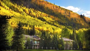 A lodge with multiple buildings, a well-maintained lawn, and a forested hillside in the background. - Walk to Vail Village Restaurants,  Shops & Lifts - Epic Views, Top Rated Condo! (Vail)