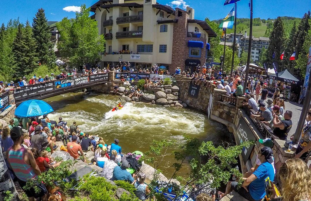A riverside event with spectators, a raft, and a building with balconies.