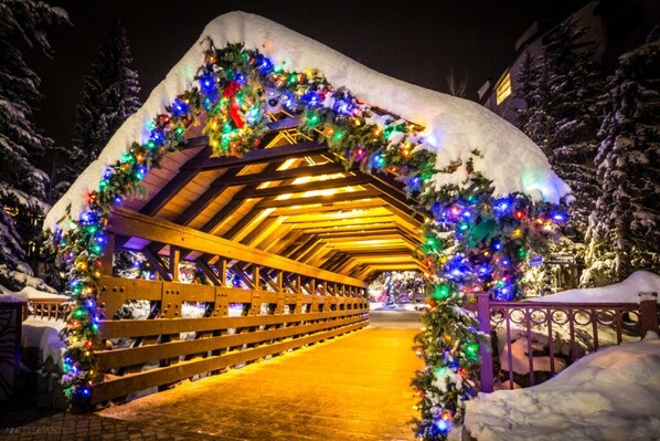 A snow-covered wooden bridge with a roof, decorated with colorful lights and garlands.