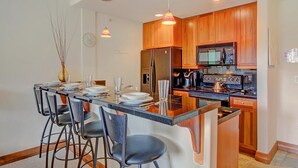 A modern kitchen with a central island, bar stools, wooden cabinets, stainless steel appliances, and pendant lighting. - Free SkyCard Act-Fitness Center, Gas Fireplace - Highland Greens Lodge 305 (Breckenridge)
