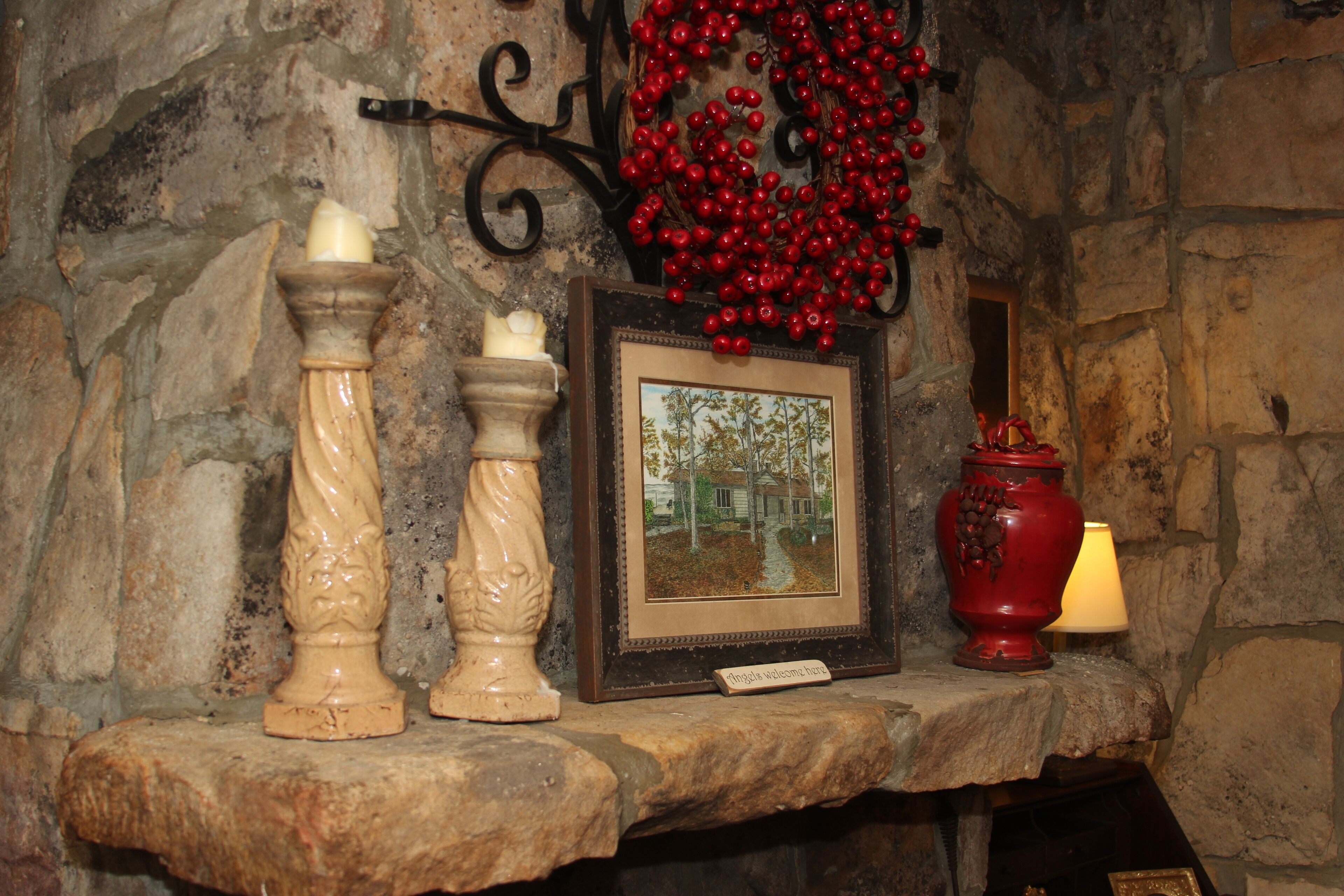 A stone fireplace with a framed picture, two candles, and a red vase.