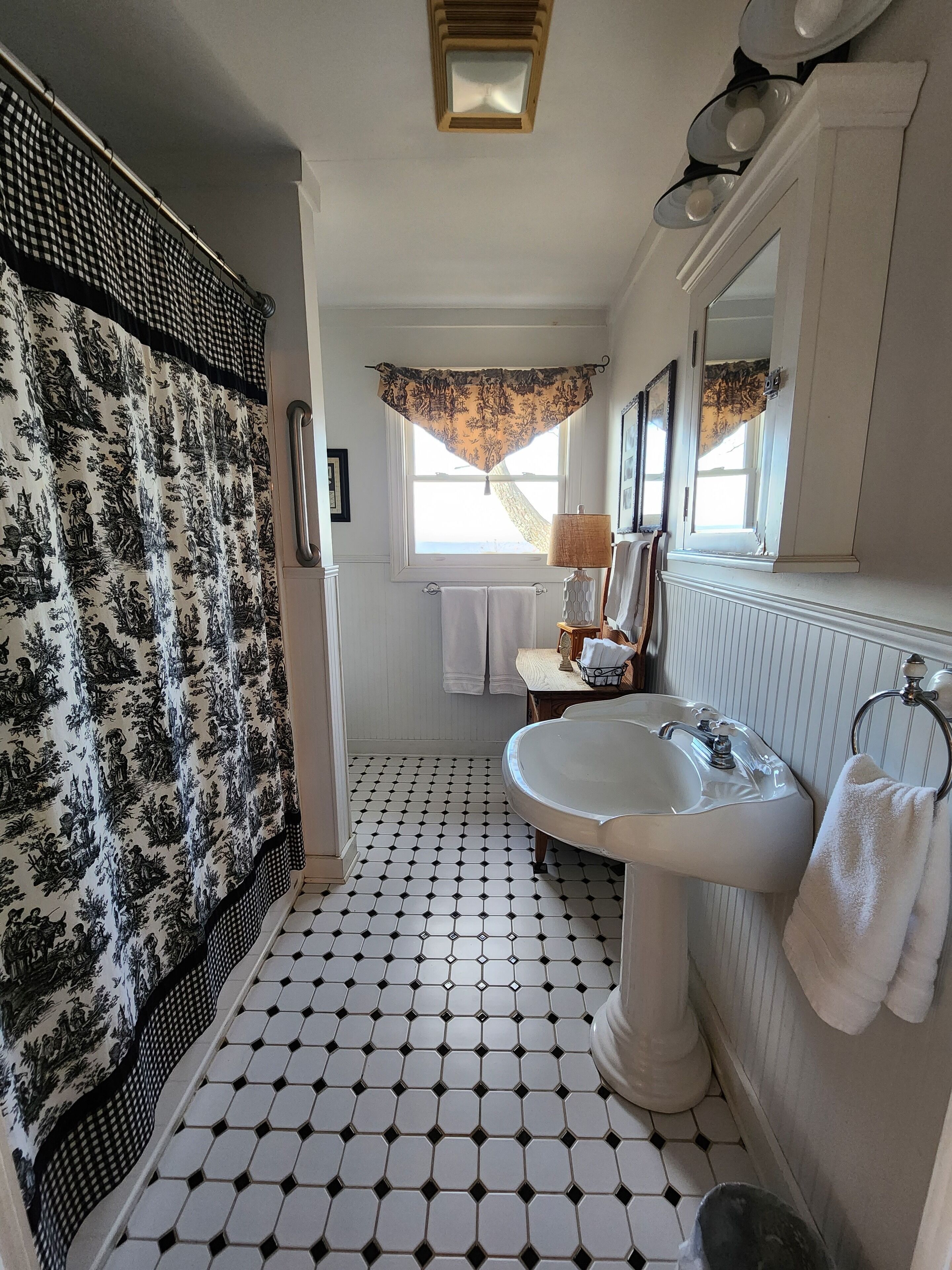 Un baño con suelo de baldosas blanco y negro, un lavabo blanco y una cortina de ducha con estampado floral.