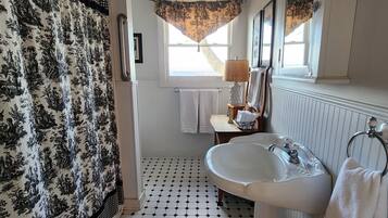Un baño con suelo de baldosas blanco y negro, un lavabo blanco y una cortina de ducha con estampado floral.
