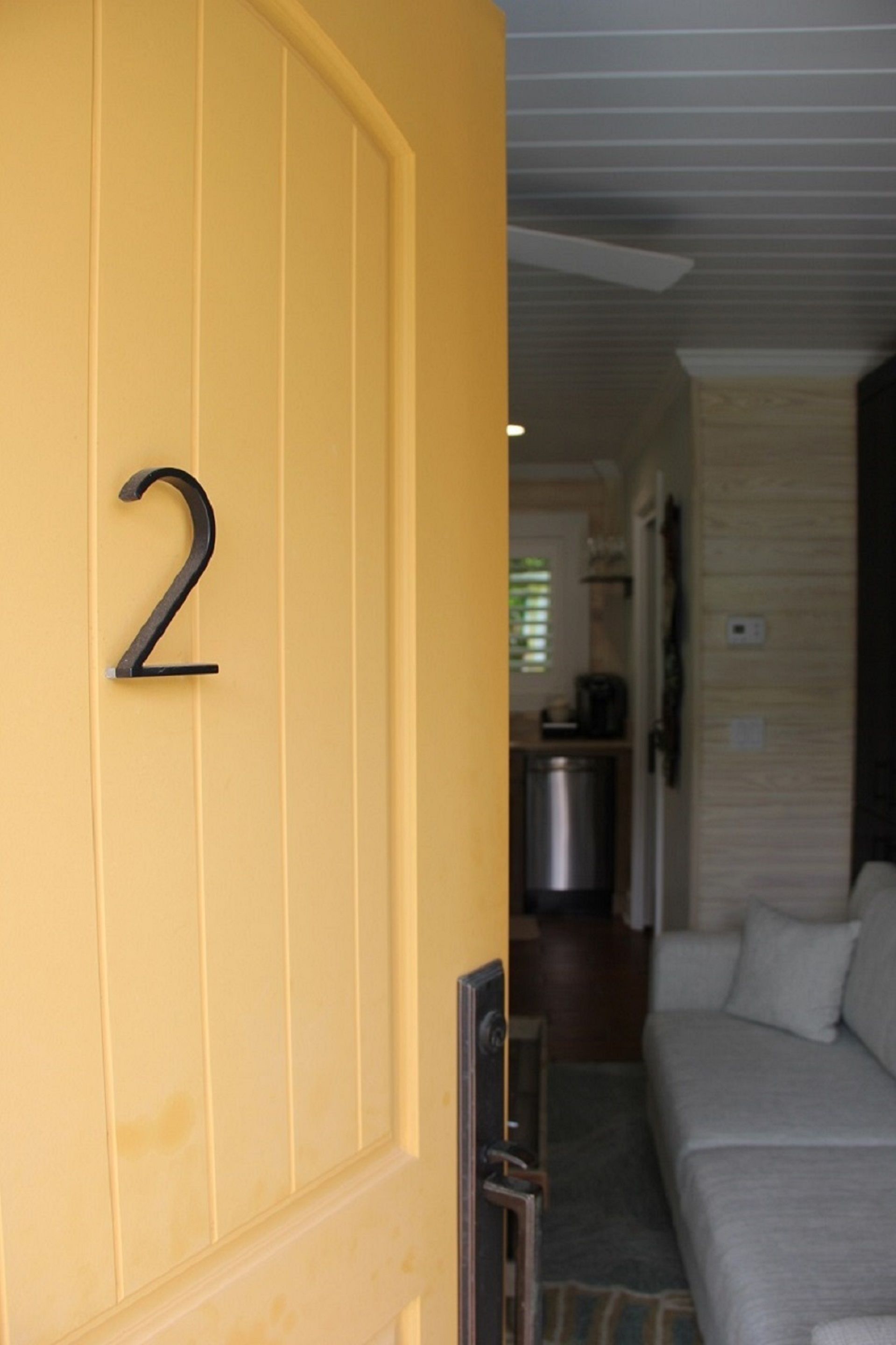 A yellow door with the number 2, leading to a living area with a sofa and a kitchen in the background.