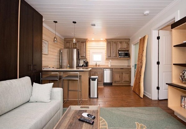 A compact living space with a kitchenette, a sofa, a coffee table, and a trash bin. - 6West Beach Cottages (Madeira Beach)