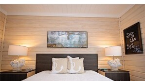 A bedroom with a large bed, two nightstands, and a wall-mounted painting.