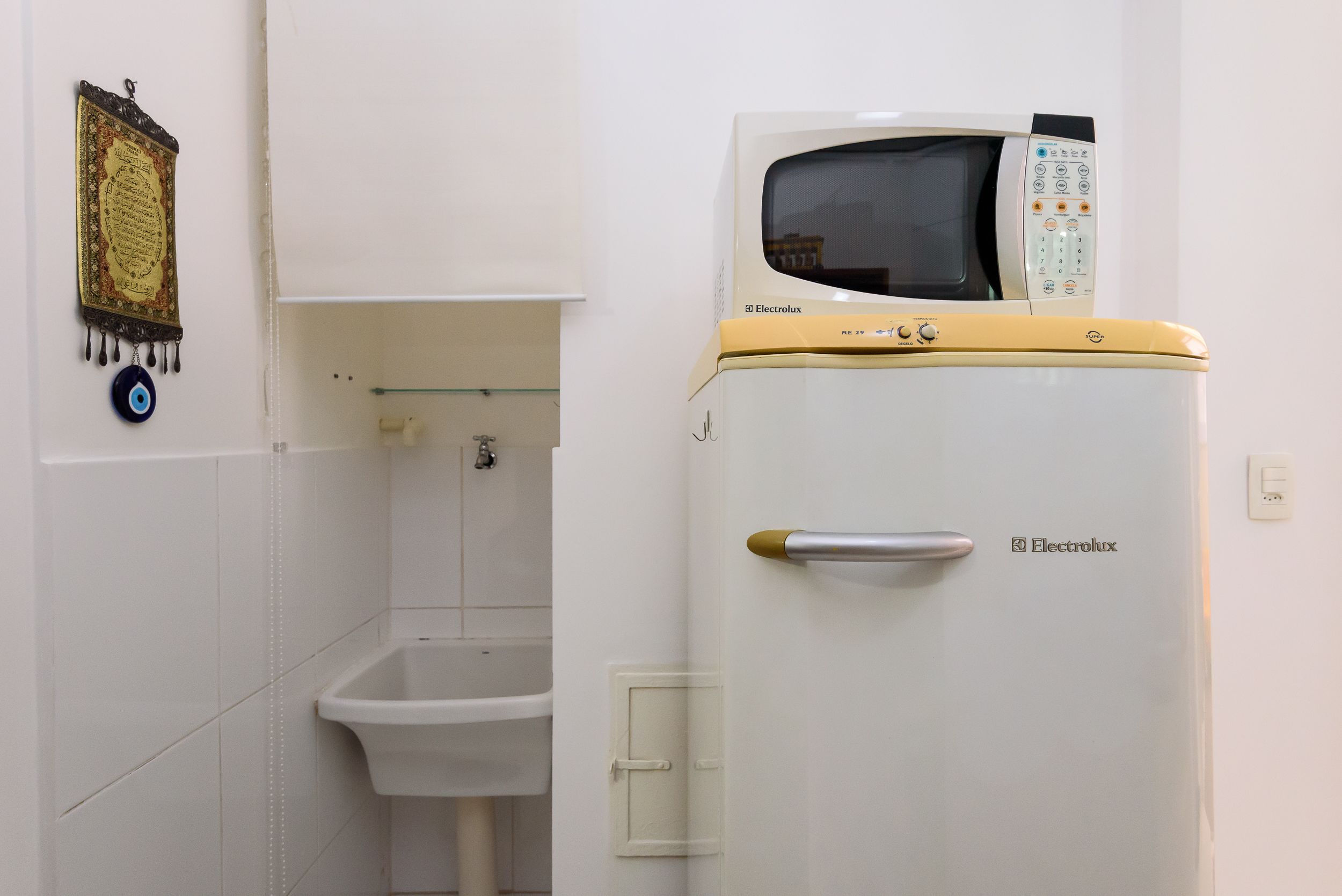 Une salle de bain avec un lavabo blanc, des toilettes et un réfrigérateur Electrolux blanc et jaune.