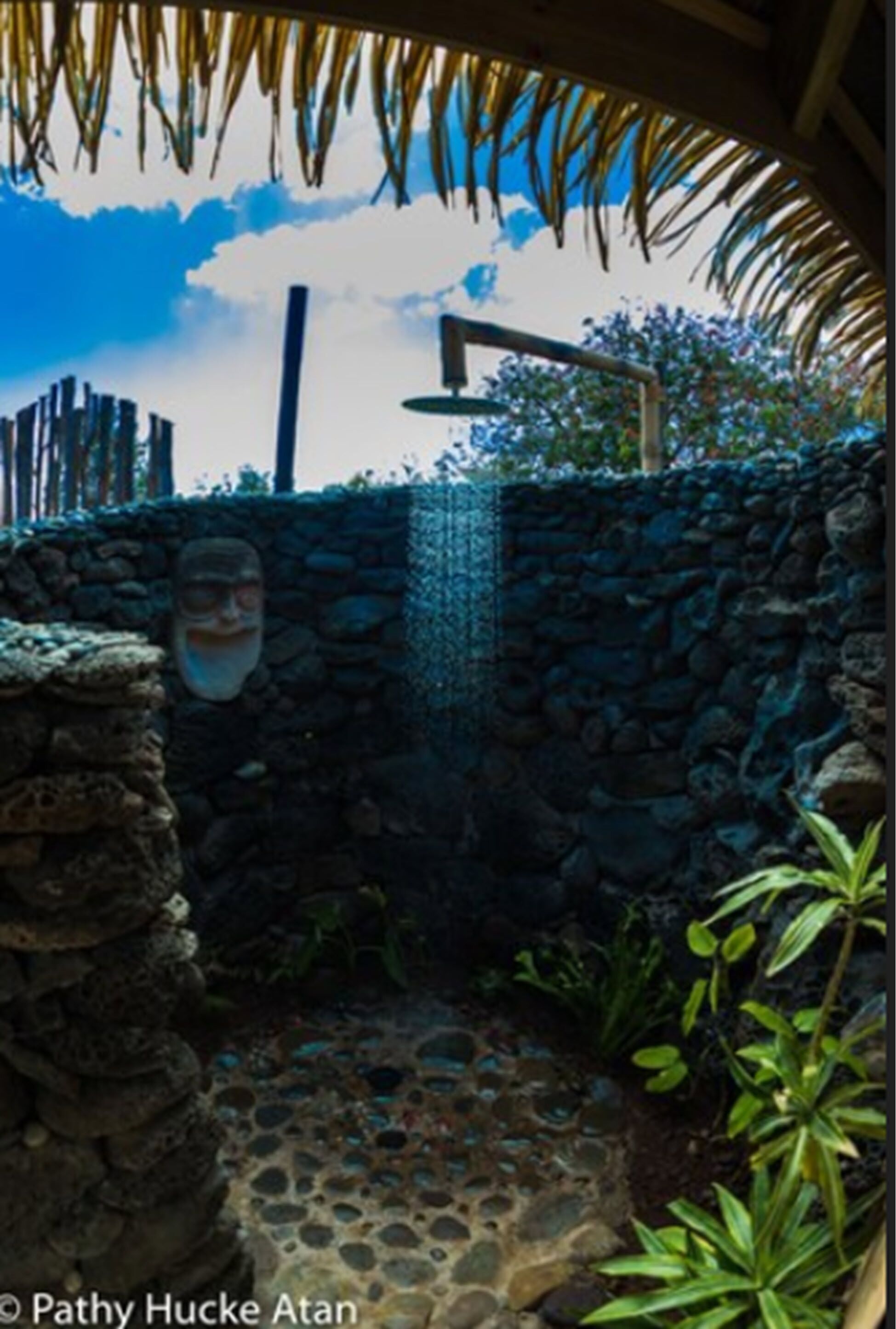 A stone wall with a decorative mask, a stone pathway, and a thatched roof structure.