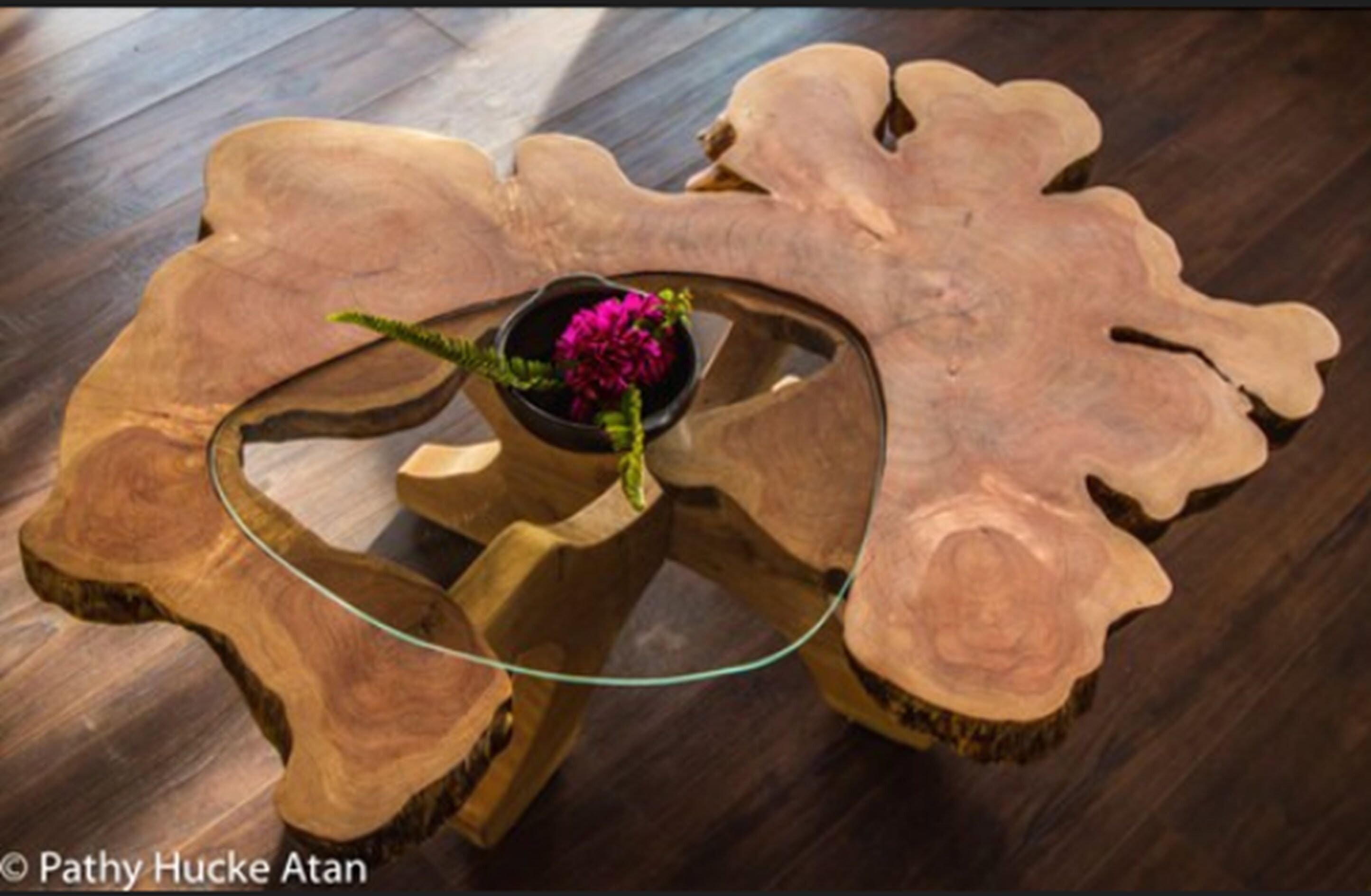 Una mesa de centro de madera con tapa de vidrio y un cuenco pequeño con flores.