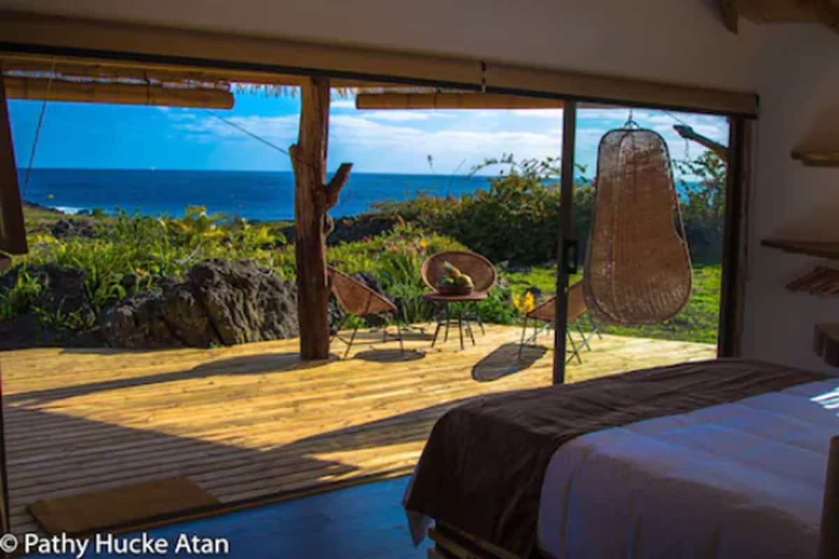 Ein Schlafzimmer mit einem großen Bett, Meerblick und einer Holzterrasse mit Stühlen.