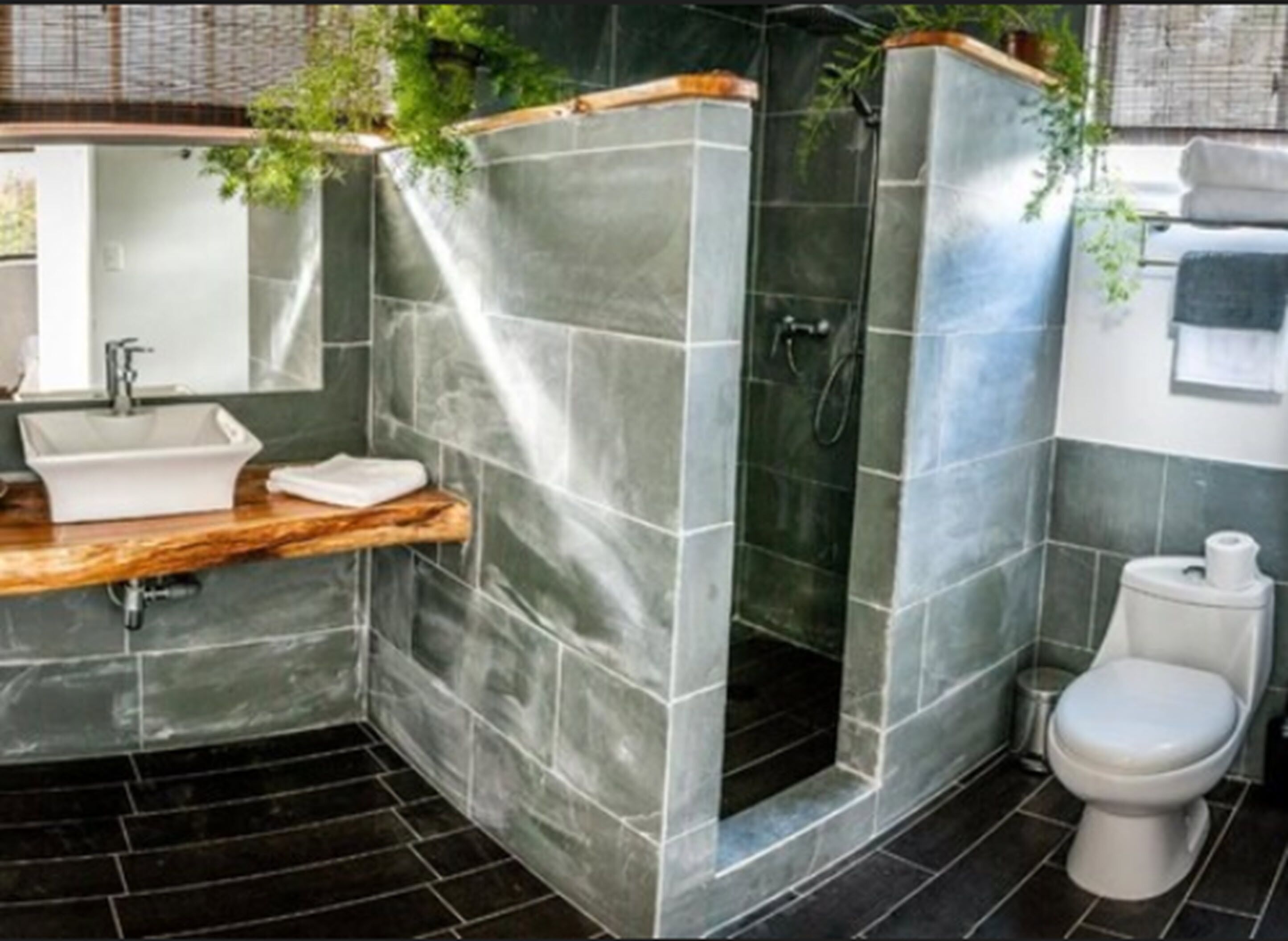 A bathroom with a sink, mirror, toilet, and shower area.
