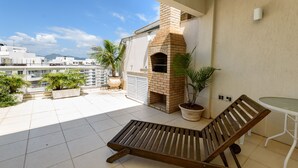 A balcony with a brick oven, potted plants, and a lounge chair. - Omar do Rio - Apartamento CobR (Rio de Janeiro)