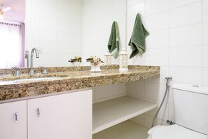 Un baño con azulejos blancos, encimera de granito, un inodoro y dos toallas verdes colgadas en la pared.