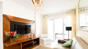 A modern living room with a flat-screen TV, a wooden entertainment unit, a white sofa, a green pillow, and a chandelier. - Omar do Rio - Apartamento CobR (Rio de Janeiro)