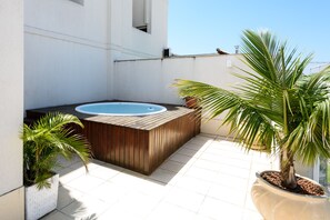 Una terraza en la azotea con jacuzzi, plantas en macetas y suelo de baldosas.