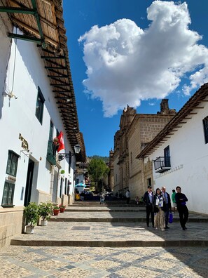 A narrow street with buildings on either side, steps leading up to a higher level, and a clear blue sky with clouds. - Valle del Inca (Cajamarca)