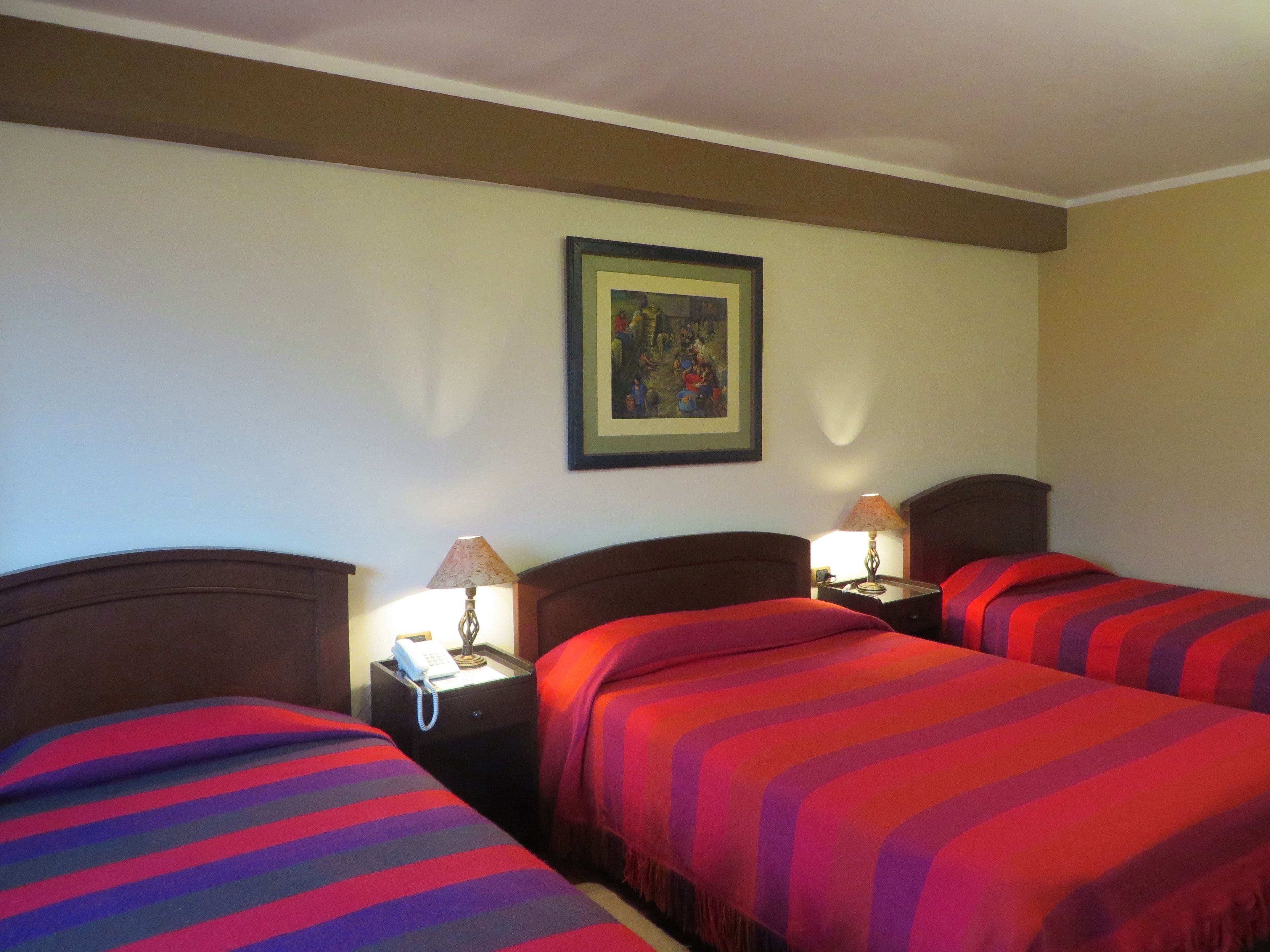 Una habitación de hotel con dos camas, cada una con una manta a rayas, una mesita de noche con una lámpara y un cuadro en la pared.