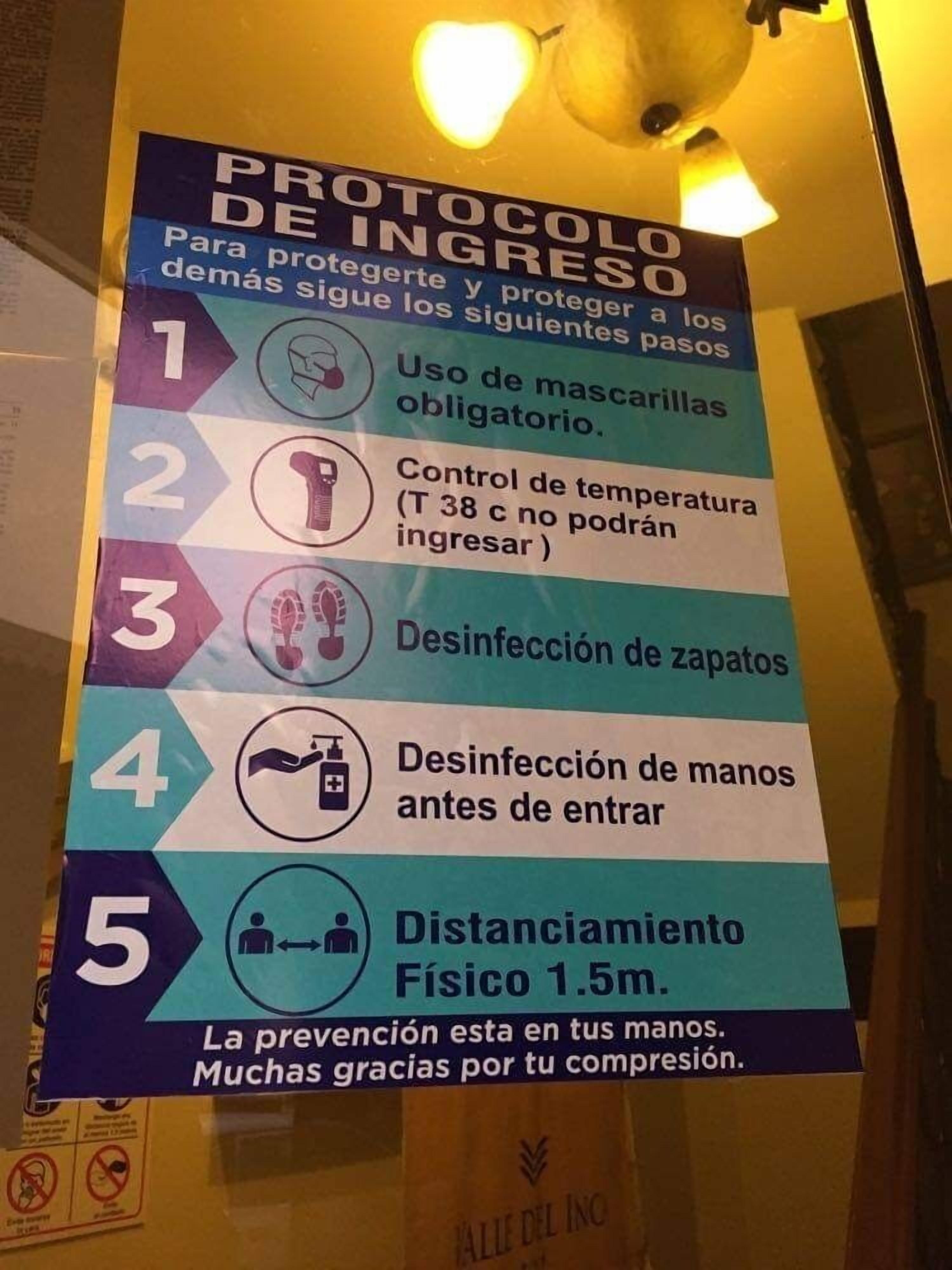 A sign listing entry protocols for a facility, including mask usage, temperature checks, glove and hand disinfection, and physical distancing.