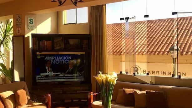 A living room with a sofa, coffee table, and TV. There is a window with a view of a building. - Valle del Inca (Cajamarca)